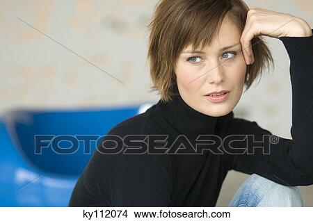 Picture - Young woman sitting on the floor, looking away. Fotosearch