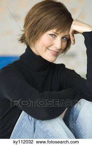 Stock Image - Young woman sitting on the floor, smiling for the camera. Fotosearch