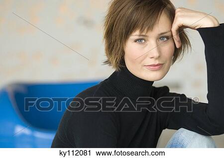 Stock Image - Young woman sitting on the floor, looking at the camera. Fotosearch