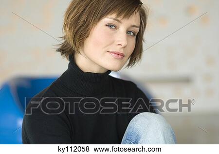 Stock Photo - Young woman sitting on the floor, looking at the camera. Fotosearch