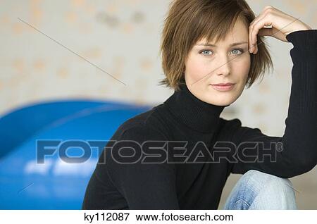 Stock Photo - Young woman sitting on the floor, looking at the camera. Fotosearch