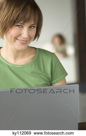 Stock Photo - Young woman using laptop computer, smiling for the camera. Fotosearch