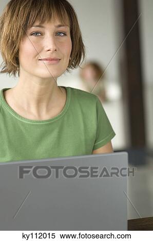 Young woman using laptop computer, looking at the camera View Large Photo Image Stock Photography - Young woman using laptop computer, looking at the camera. Fotosearch
