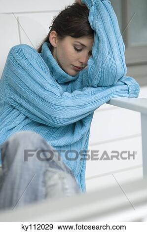 Stock Photo - Young woman with blue pullover, resting her head on her arms, outdoors. Fotosearch