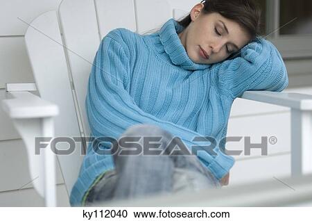 Stock Image - Young woman with blue pullover, sleeping on a chair resting her head on her arm, outdoors. Fotosearch