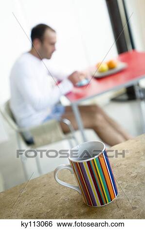 Stock Photograph - Man at breakfast table, cup in foreground. Fotosearch