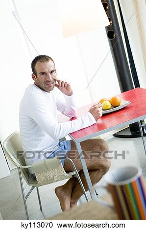 Stock Image - Man at breakfast table, looking at the camera, cup in foreground. Fotosearch
