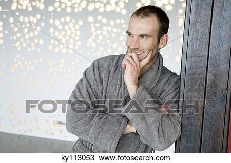 Stock Image - Man in grey bathrobe, leaning against wall. Fotosearch