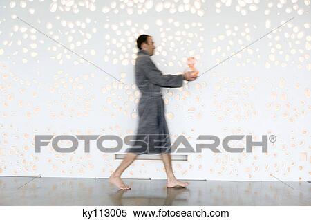 Stock Photography - Man in grey bathrobe, walking, holding a vase, side view. Fotosearch