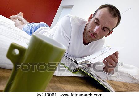 Man lying in bed, reading a book, mug in foreground View Large Photo Image Stock Image - Man lying in bed, reading a book, mug in foreground. Fotosearch