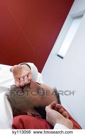 Stock Photograph - Man lying in bed, yawning. Fotosearch