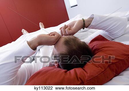 Man lying on a bed rubbing his eyes, rear view View Large Photo Image Stock Image - Man lying on a bed rubbing his eyes, rear view. Fotosearch