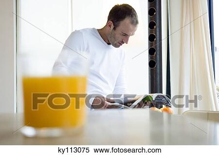 Man reading a magazine in the kitchen, orange juice in foreground View Large Photo Image Stock Photography - Man reading a magazine in the kitchen, orange juice in foreground. Fotosearch
