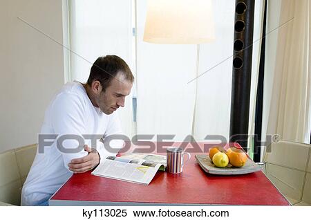 Man sitting in the kitchen, reading a magazine View Large Photo Image Stock Photography - Man sitting in the kitchen, reading a magazine. Fotosearch