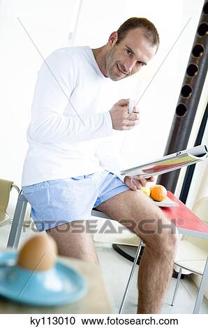 Man sitting on kitchen table, reading magazine, holding mug, boiled egg in foreground View Large Photo Image Stock Image - Man sitting on kitchen table, reading magazine, holding mug, boiled egg in foreground. Fotosearch
