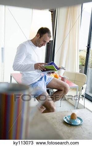 Man sitting on kitchen table, reading magazine, cup and boiled egg in foreground View Large Photo Image Stock Image - Man sitting on kitchen table, reading magazine, cup and boiled egg in foreground. Fotosearch