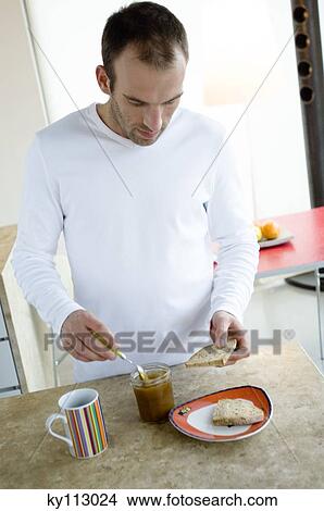 Man standing in the kitchen, spreading slice of bread with jam View Large Photo Image Picture - Man standing in the kitchen, spreading slice of bread with jam. Fotosearch