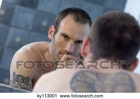 Stock Image - Tattooed man, barechested, in front of bathroom mirror. Fotosearch