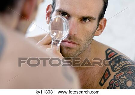 Tattooed man, barechested, looking in bathroom mirror, holding a magnifying glass View Large Photo Image Stock Image - Tattooed man, barechested, looking in bathroom mirror, holding a magnifying glass. Fotosearch