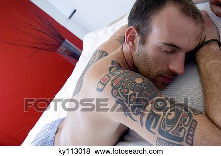 Stock Photo - Tattooed man, barechested, sleeping in bed. Fotosearch