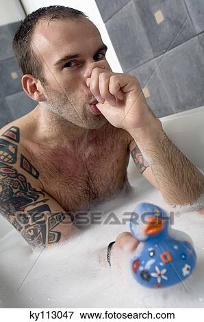 Stock Photo - Tattooed man having a bath, sucking his thumb, holding a plastic duck. Fotosearch