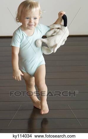 Picture - Little boy holding stuffed dog, walking on wooden floor, front view. Fotosearch