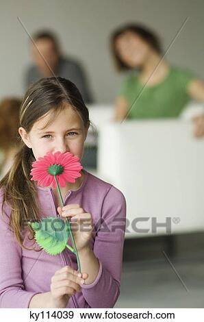 Little girl holding a plastic flower in front of her face, couple in the background View Large Photo Image Stock Photo - Little girl holding a plastic flower in front of her face, couple in the background. Fotosearch