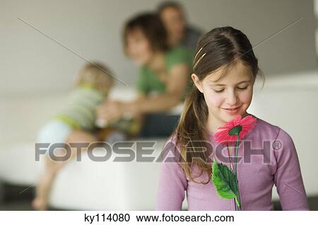 Stock Image - Little girl holding a plastic flower, couple and child in the background. Fotosearch