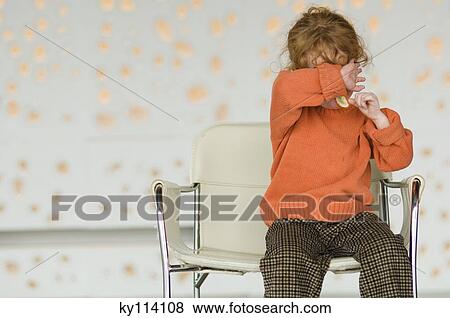 Stock Photo - Little girl sitting on a chair, covering her face with her arm. Fotosearch