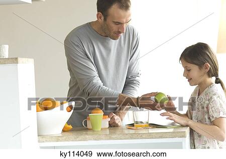 Man standing inthe kitchen, giving an apple to little girl View Large Photo Image Stock Photo - Man standing inthe kitchen, giving an apple to little girl. Fotosearch