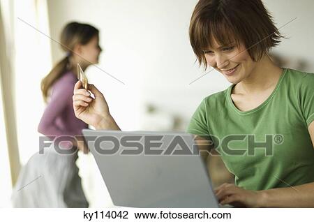Woman using laptop computer, holding a credit card, little girl in the background View Large Photo Image Stock Image - Woman using laptop computer, holding a credit card, little girl in the background. Fotosearch