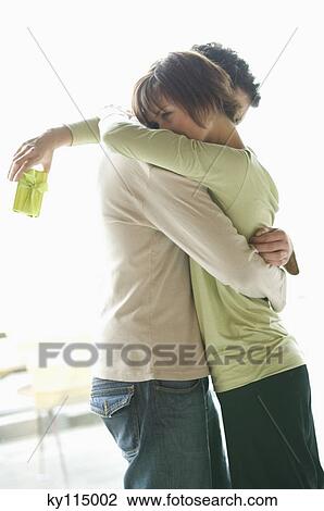 Stock Image - Couple embracing, woman holding present. Fotosearch