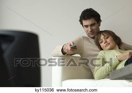 Stock Photograph - Couple lying on a sofa, watching TV. Fotosearch