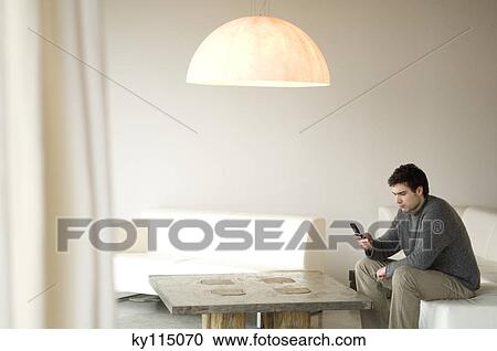 Man sitting on a sofa in living-room, using mobile phone View Large Photo Image Stock Image - Man sitting on a sofa in living-room, using mobile phone. Fotosearch