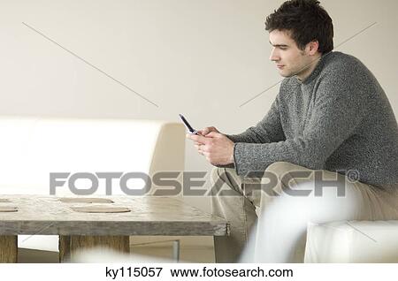 Man sitting on a sofa using a mobile phone View Large Photo Image Stock Photo - Man sitting on a sofa using a mobile phone. Fotosearch