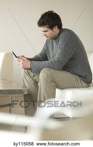 Man sitting on a sofa using a mobile phone View Large Photo Image Stock Photo - Man sitting on a sofa using a mobile phone. Fotosearch