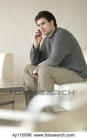 Stock Photograph - Man sitting on a sofa using a mobile phone. Fotosearch