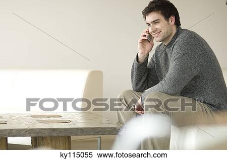 Man sitting on a sofa using a mobile phone View Large Photo Image Stock Photography - Man sitting on a sofa using a mobile phone. Fotosearch