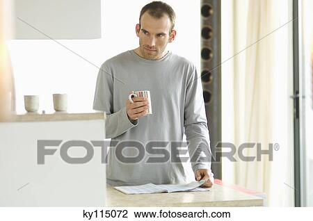 Man standing in the kitchen, holding mug View Large Photo Image Stock Image - Man standing in the kitchen, holding mug. Fotosearch