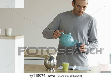 Man standing in the kitchen, pouring tea into a glass View Large Photo Image Picture - Man standing in the kitchen, pouring tea into a glass. Fotosearch