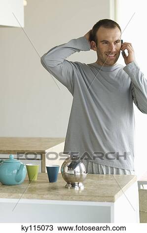 Man standing in the kitchen, using a mobile phone View Large Photo Image Stock Image - Man standing in the kitchen, using a mobile phone. Fotosearch