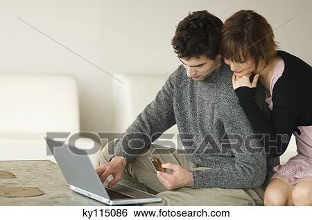 Man using laptop computer and holding credit card, woman resting on his shoulder View Large Photo Image Stock Photograph - Man using laptop computer and holding credit card, woman resting on his shoulder. Fotosearch