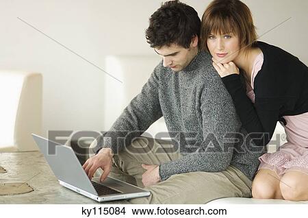 Picture - Man using laptop computer, woman resting on his shoulder. Fotosearch
