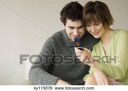 Stock Photo - Smiling couple looking at mobile phone. Fotosearch
