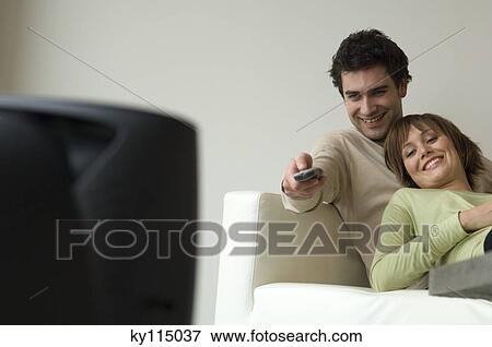 Smiling couple lying on a sofa, watching TV View Large Photo Image Stock Photo - Smiling couple lying on a sofa, watching TV. Fotosearch