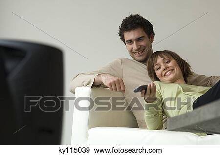 Stock Photo - Smiling couple lying on a sofa, watching TV. Fotosearch