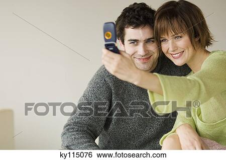 Smiling couple taking picture with camera phone View Large Photo Image Stock Photograph - Smiling couple taking picture with camera phone. Fotosearch