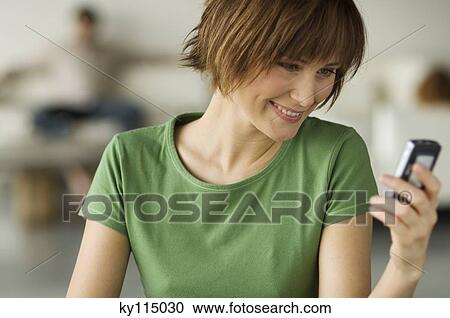 Smiling woman holding mobile phone, man in the background View Large Photo Image Stock Image - Smiling woman holding mobile phone, man in the background. Fotosearch