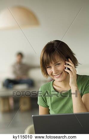 Smiling woman using laptop computer and mobile phone, man in the background View Large Photo Image Stock Image - Smiling woman using laptop computer and mobile phone, man in the background. Fotosearch