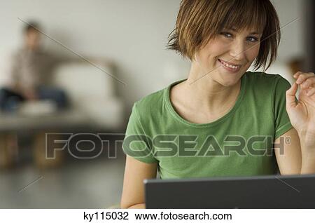 Smiling woman using laptop computer, man in the background View Large Photo Image Stock Image - Smiling woman using laptop computer, man in the background. Fotosearch